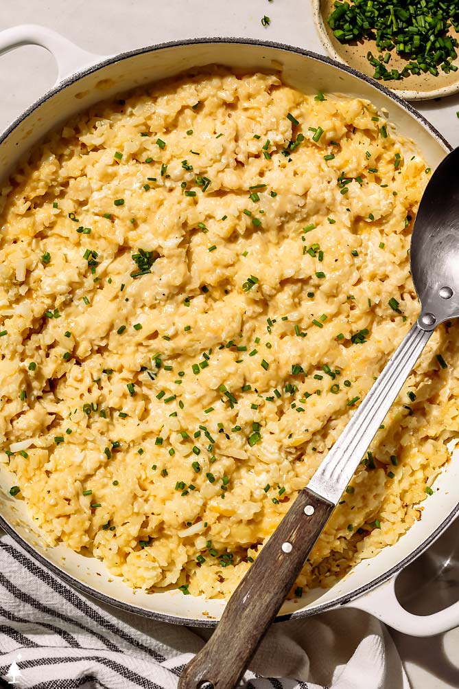 cheesy cauliflower rice recipes in a pan with a spoon and chives