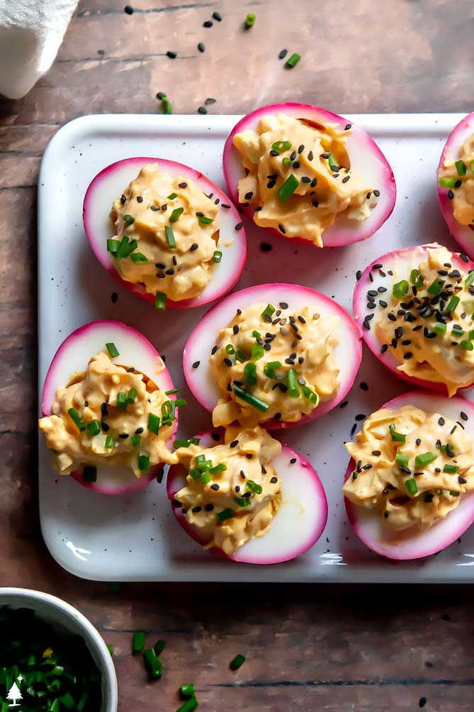beet pickled deviled eggs on a platter with chives and seeds