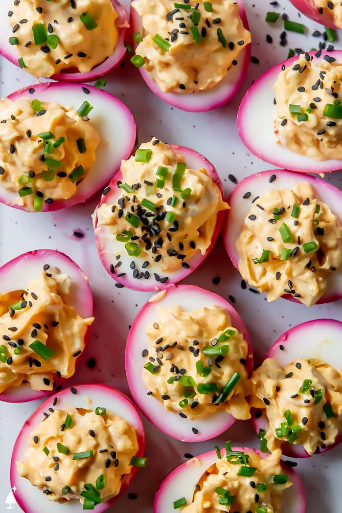 beet deviled eggs on a platter with chives and seeds