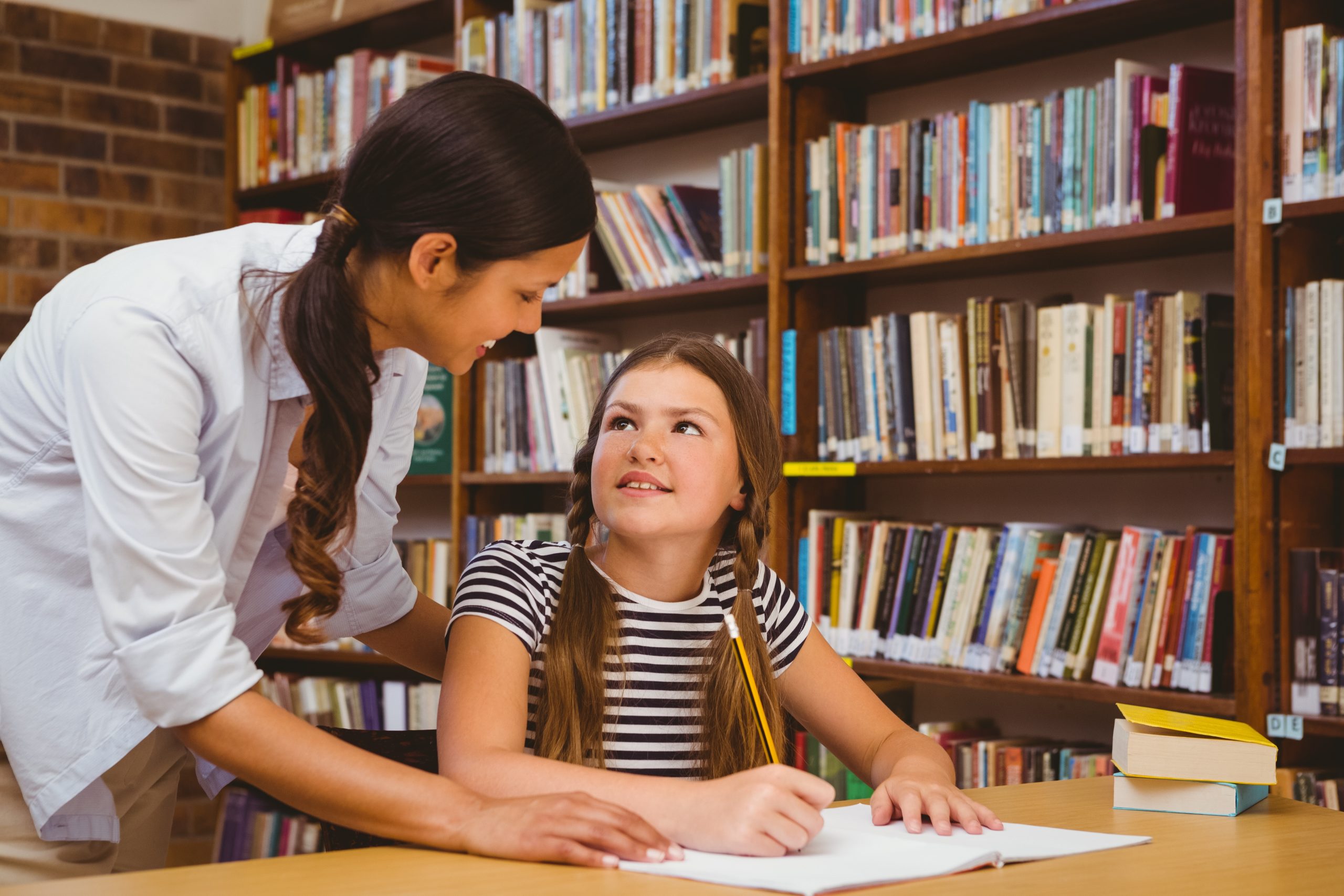 Teacher assisting girl with homework in library Themba Tutors