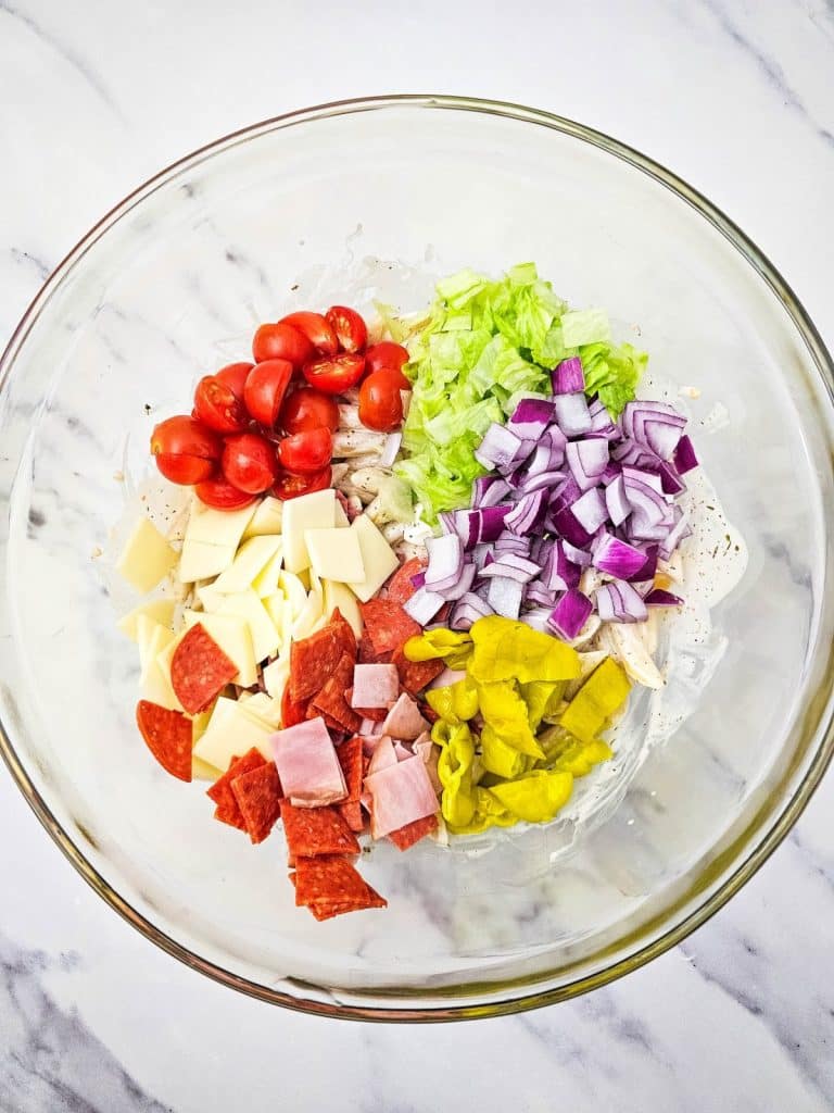 italian hoagie pasta salad ingredients in a large glass mixing bowl