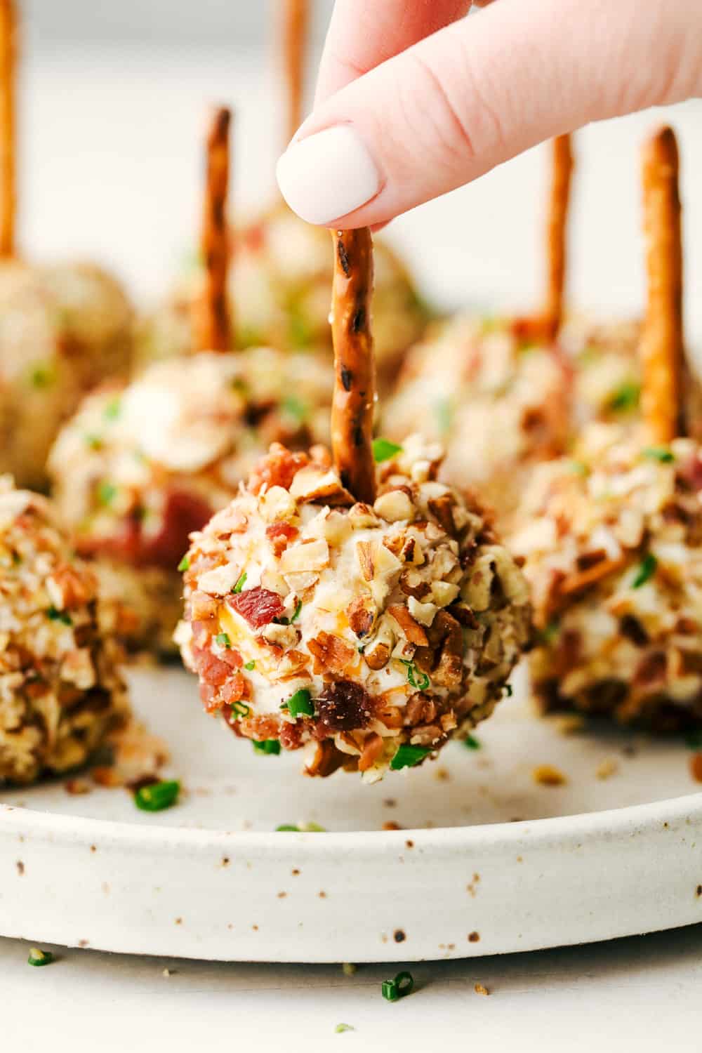 Bacon Ranch Cheese Ball Bites are delicious appetizers loaded with shredded cheese, a pop of color from the green onion, cooked bacon chunks mixed with black olives and pecans all rolled together in a tight ball with a pretzel on top. An elegant appetizer to enjoy this holiday season! Bacon ranch cheese ball bites with a pretzel on top.
