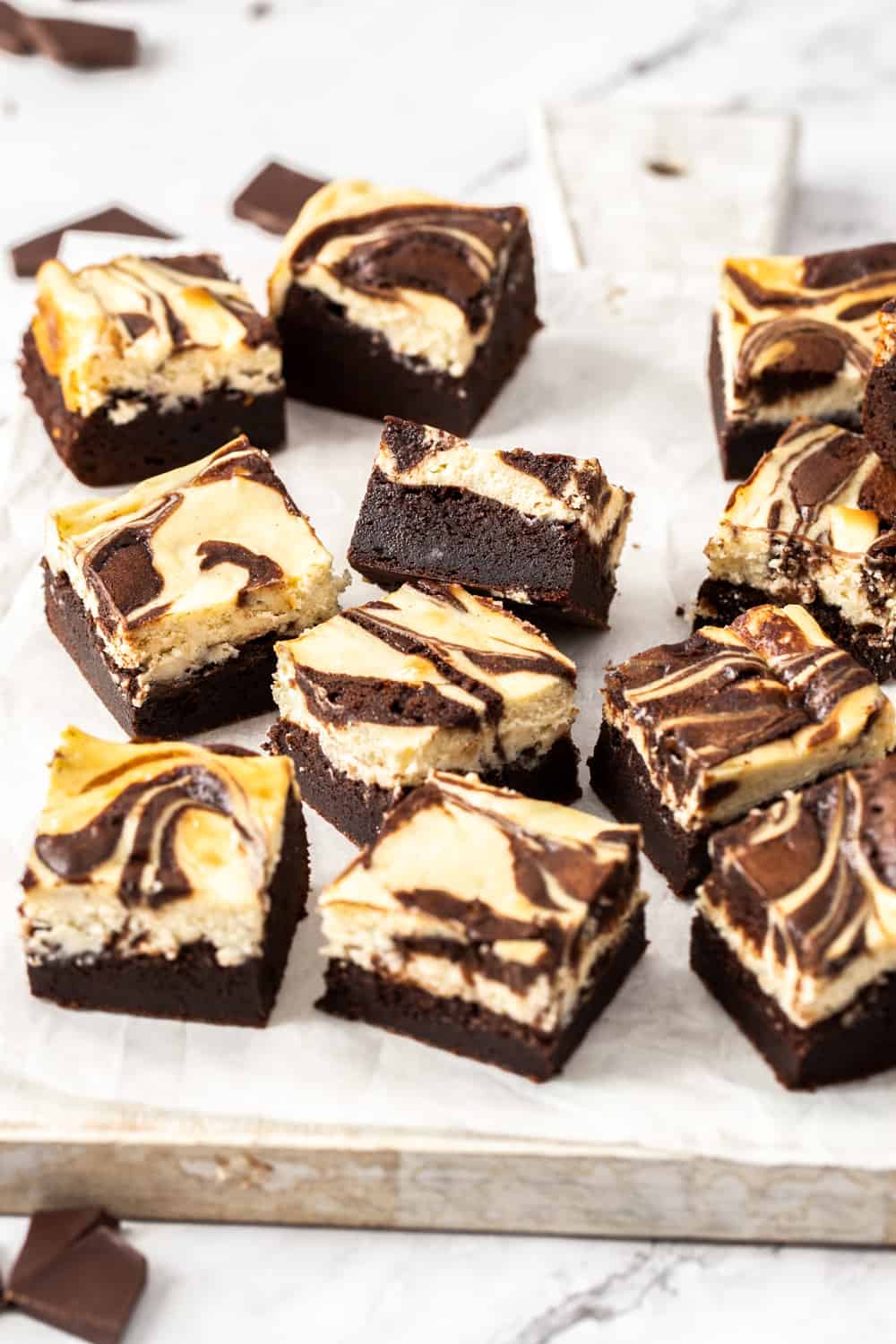 Super fudgy brownies, topped with a layer of creamy cheesecake, these deliciously indulgent Cheesecake Brownies are easy to make in just two bowls. A batch of brownies on a white wooden board.