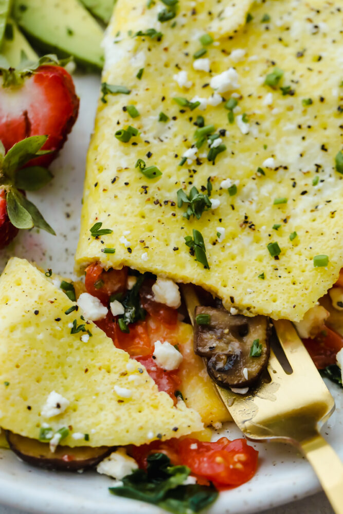 Savory breakfast omelets are so classic and my go to for a home run breakfast! Quick, easy, and delicious, this healthy breakfast option will leave you feeling full and satisfied! A fully cooked omelet on a plate with a fork cutting into it.