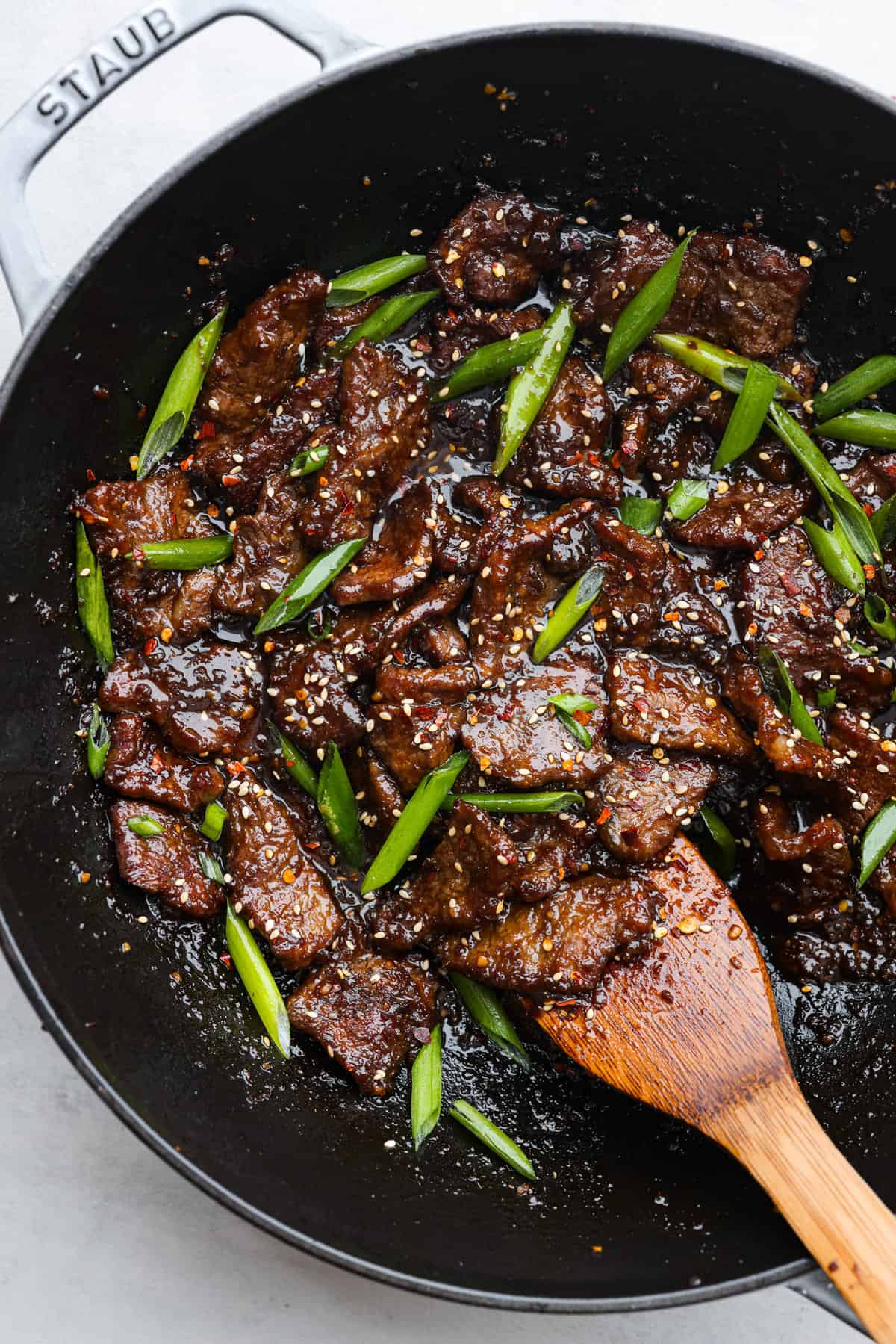 This Mongolian beef is crazy tender with a crispy seared edge that gets coated in a bold sticky sauce. It's way better than P.F. Changs and so easy to make at home! Top-down view of cooked beef and green onions in a skillet.