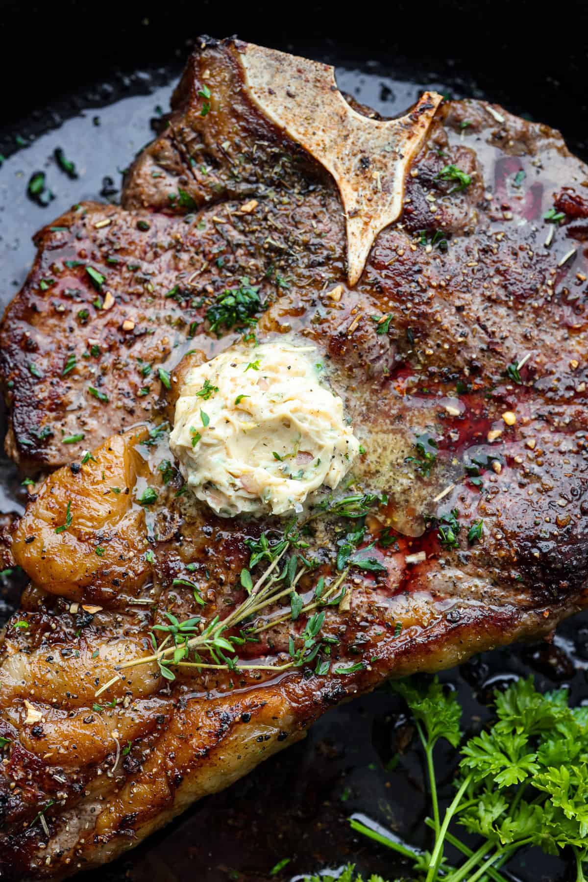 Indulge in the ultimate T-bone steak experience with this recipe! It takes an already awesome cut of meat and cooks it to perfection. The mix of olive oil, spices, and a hot skillet gives you a beautifully seared crust. Top it off with some garlic butter and fresh herbs, then you have the perfect dessert ready for any occasion! Top-down view of steak topped with butter and herbs.