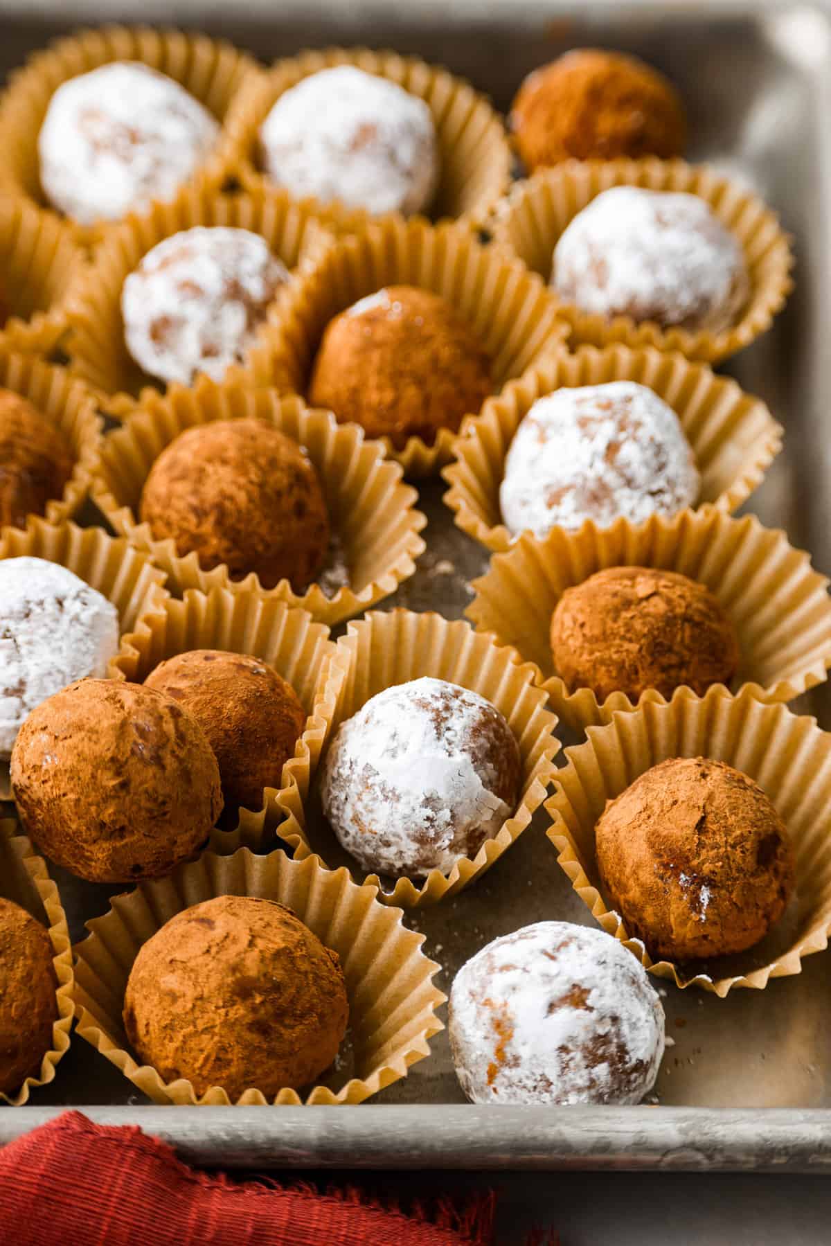 Easy and impressive rum balls are perfect for the holidays! Vanilla wafer crumbs, powdered sugar, cocoa powder, and rum create a truffle-like consistency bursting with rich flavors. A simple bite-sized dessert that every party needs! Close side view of rum balls in mini muffin cups.