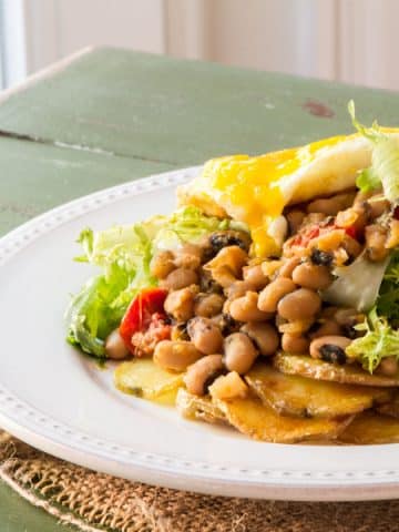 A plate of roasted potatoes topped with black-eyed peas, frisée and an egg.