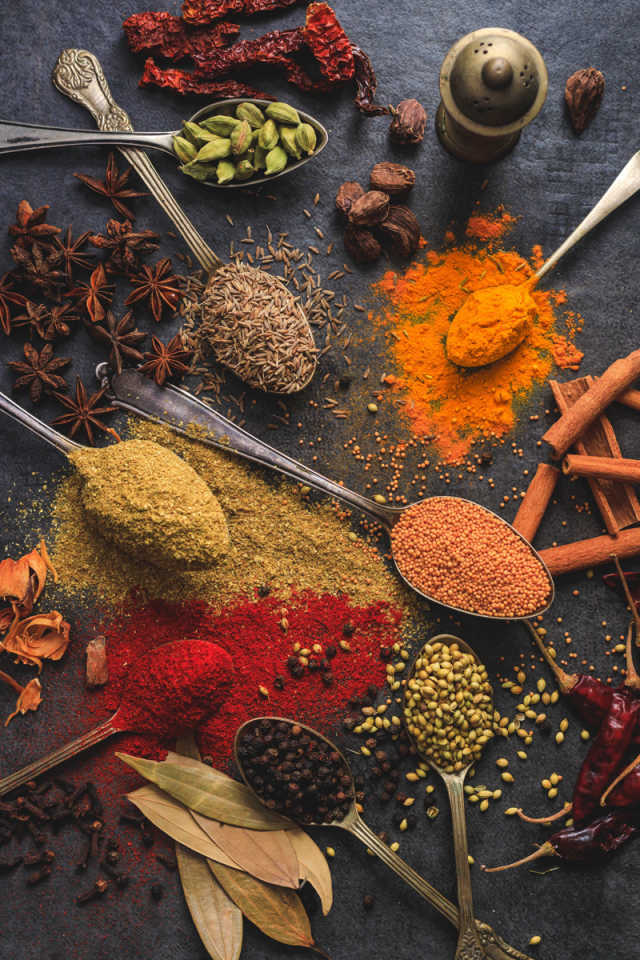 Various colorful spices on a table, some in spoons.