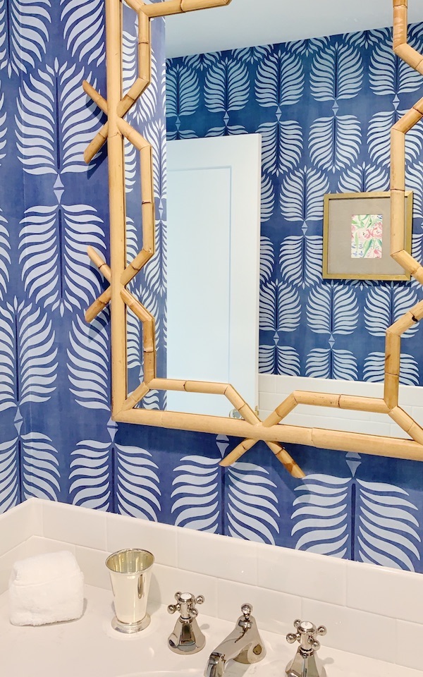 Blue leaf print wallpaper in bathroom with rattan mirror.