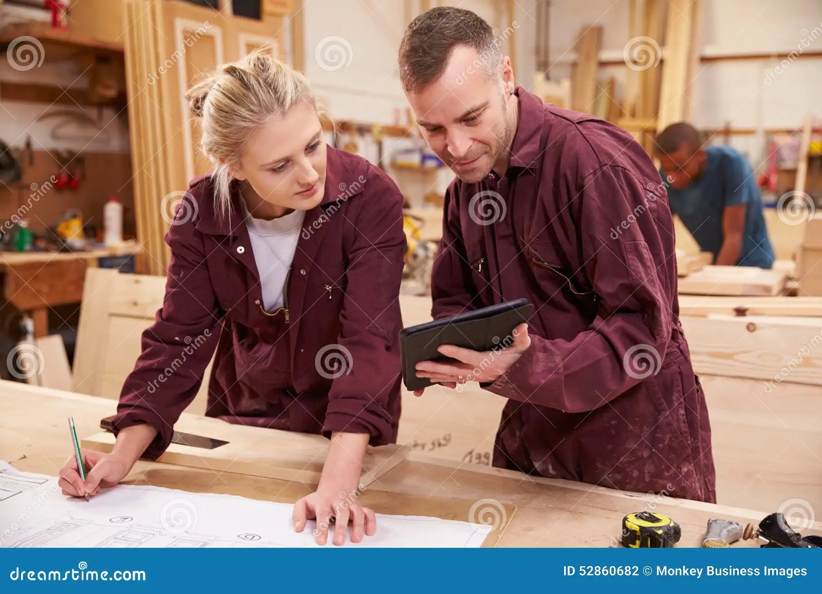 Carpenter with Apprentice Looking at Plans in Stock Photo