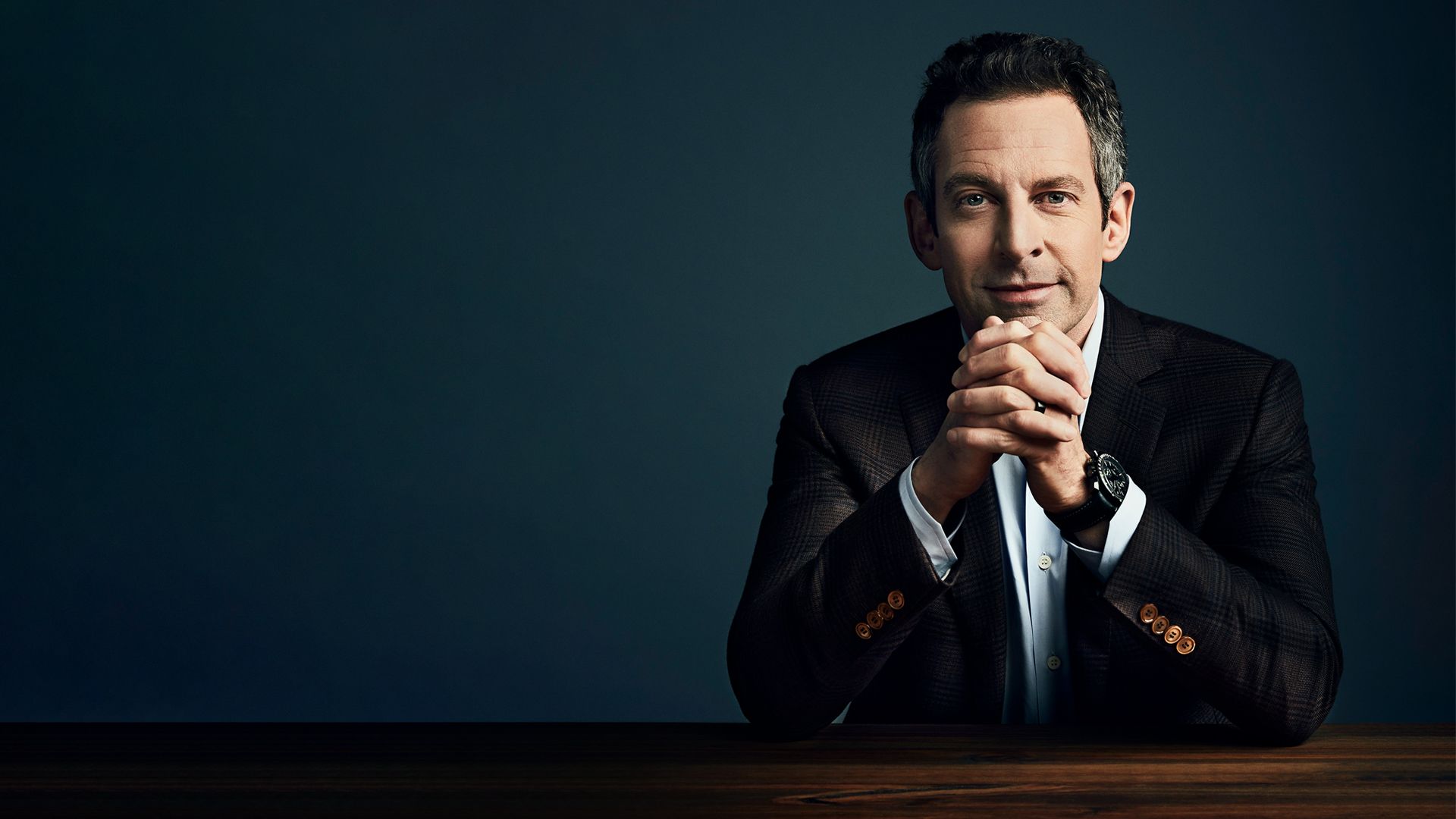 Sam Harris in a sport coat, leaning on a table.