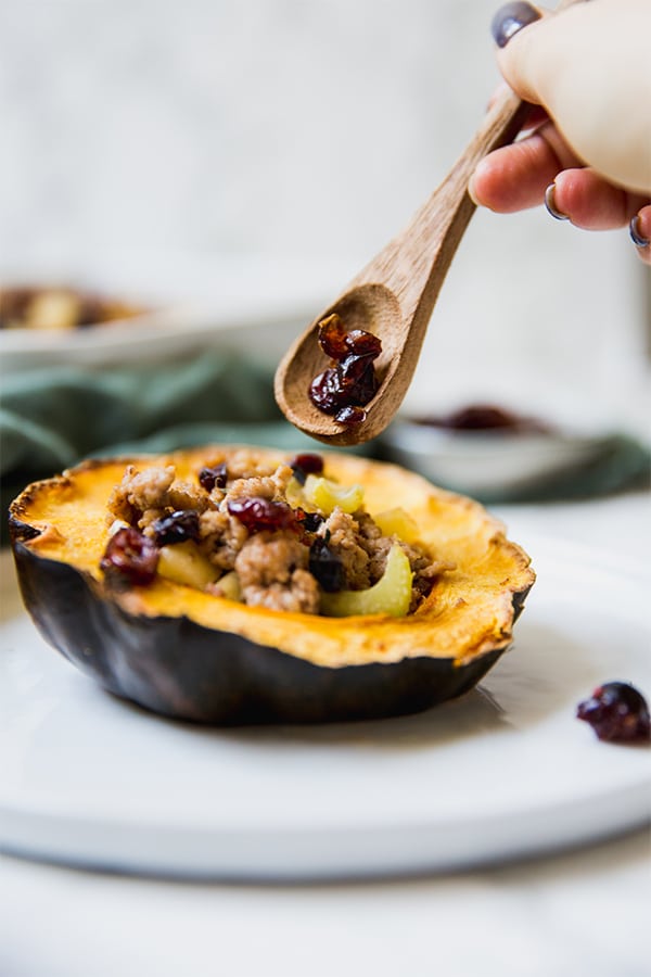 A wooden spoon putting some stuffing into an acorn squash.