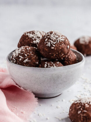 A white bowl filled with chocolate collagen protein bowls with coconut on top.