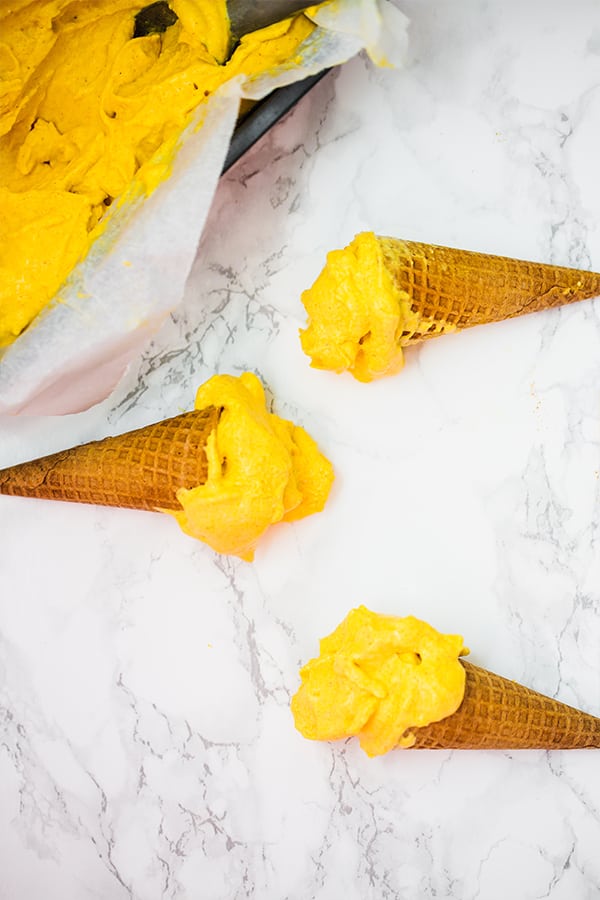 Three ice cream cones of mango turmeric ice cream lying on a counter.
