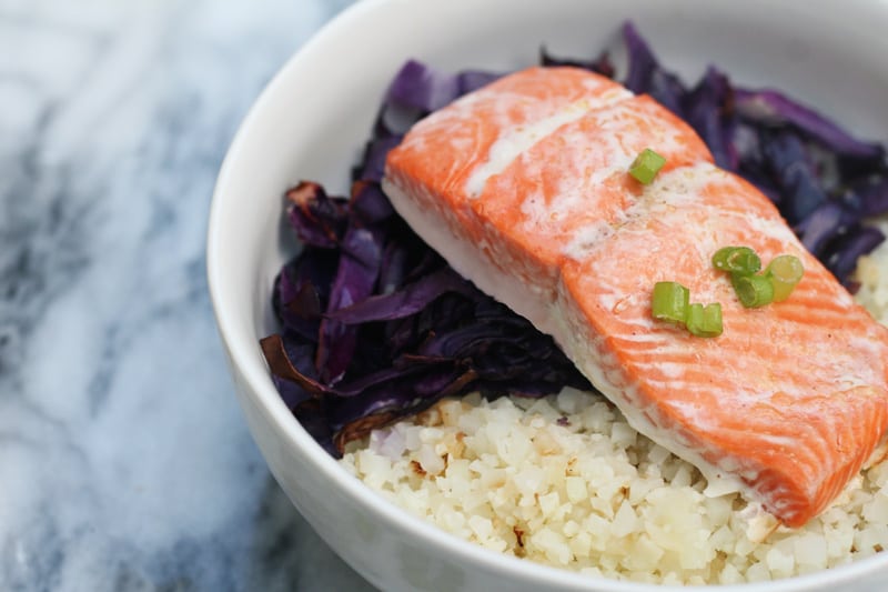 A bowl with cabbage, cauliflower rice, and salmon in it.