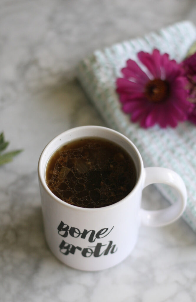 A cup of bone broth in a mug next to some flowers.