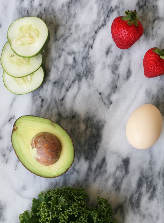 Strawberries, cucumber, egg, and avocado on a countertop.