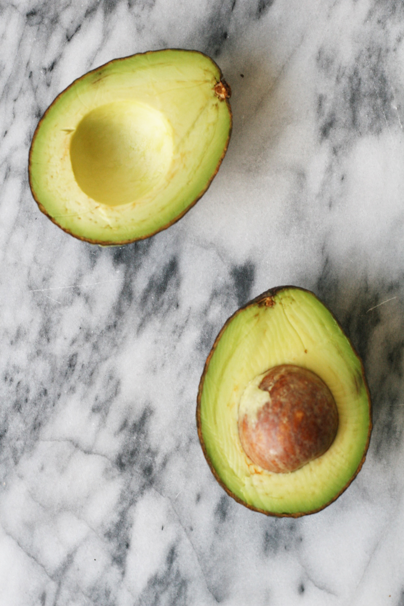 Marble background with an avocado cut in half, facing up.