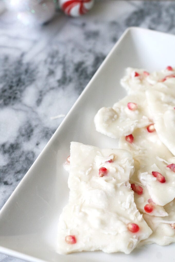 A white ceramic dish with peppermint bark topped with pomegranate seeds on it.