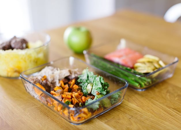 A table with two containers of meal prep and an apple on it.