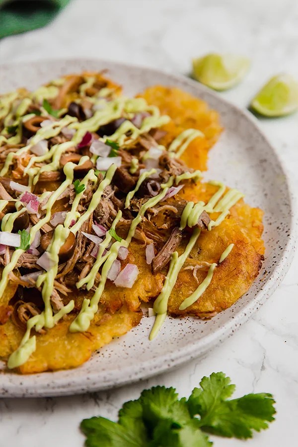 A white plate with tostone carnitas nachos on it.