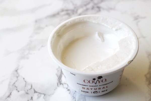 A countainer of Coyo Coconut yogurt with the top off sitting on a counter.