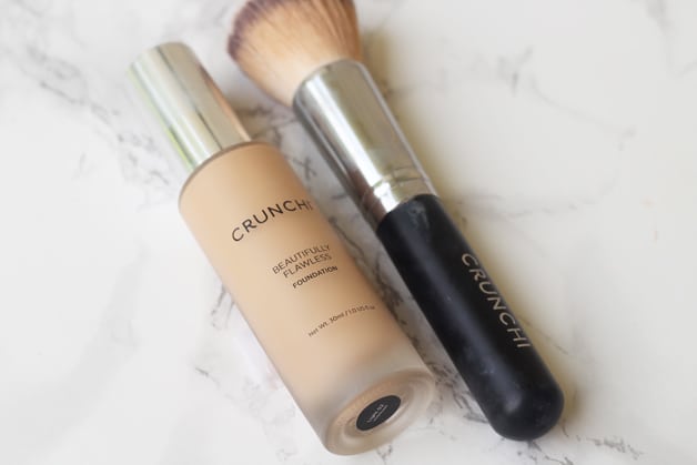 A bottle of foundation and a brush lying next to each other on a counter.