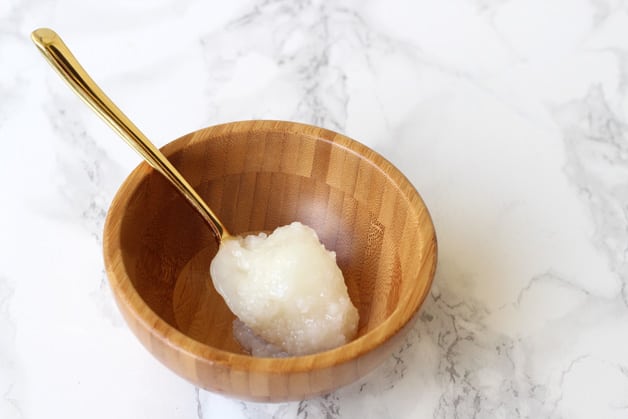 A small wooden bowl with a spoon filled with coconut oil in it.