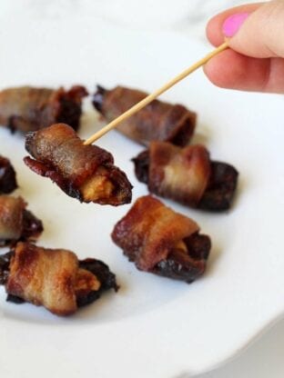 A plate with bacon wrapped dates and with a tooth pick picking one of them up.