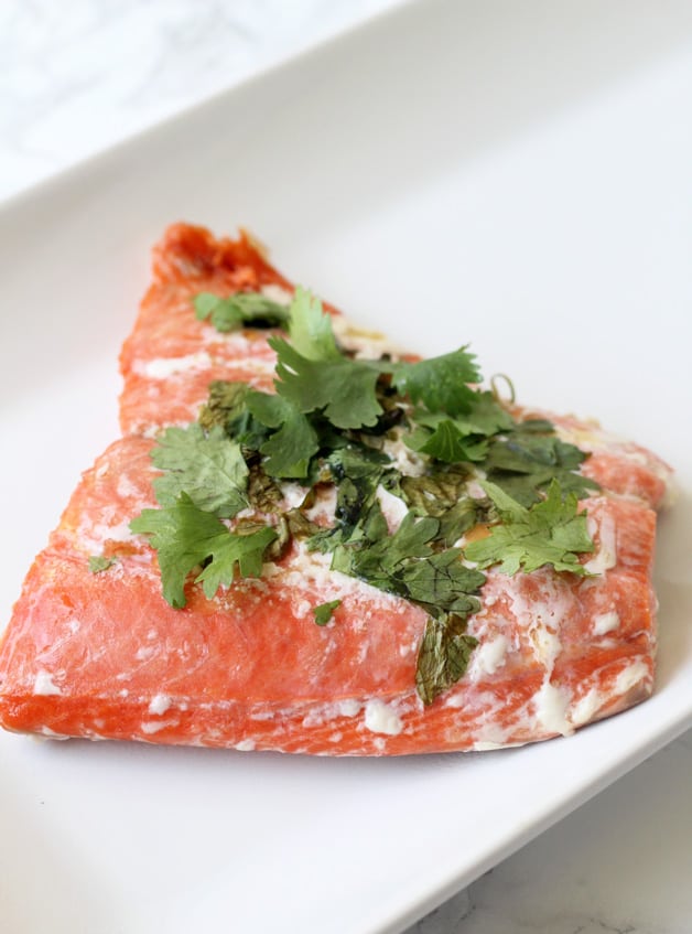 A piece of salmon topped with cilantro after cooking sitting on a white plate.