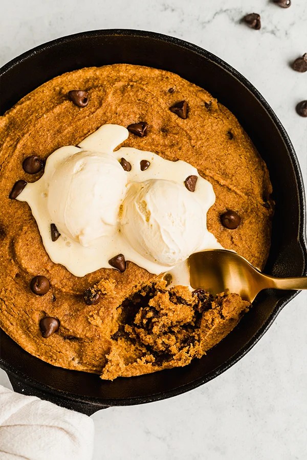 Spoon scooping from a pumpkin chocolate chip cookie in a skillet.