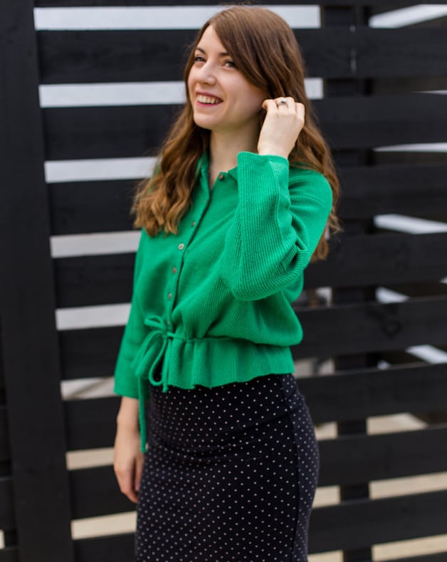 A shot of Michelle in a green sweater with a black fence behind her.