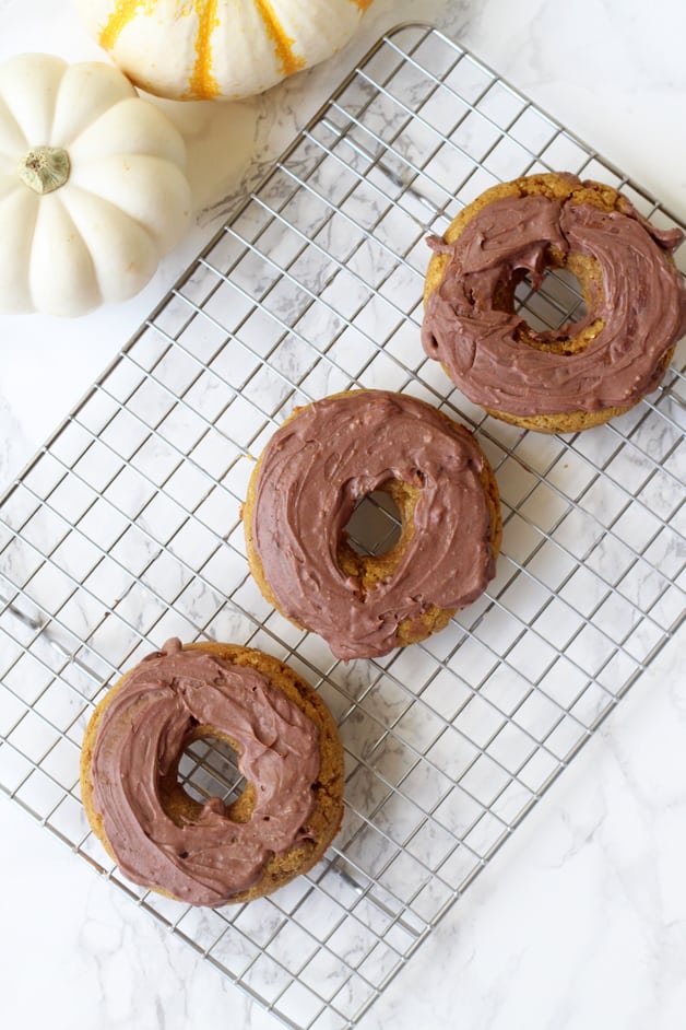 Three pumpkin donuts frosted sitting on a metal cooling rack.