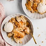 Two bowls filled with apple crisp and coconut ice cream and a spoon.