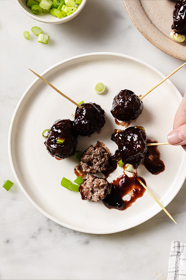 A plate with cocktail meatballs with toothpicks.