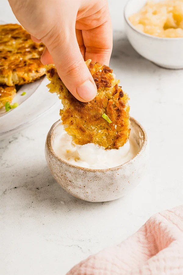 Person dipping a sweet potato latke into sauce.
