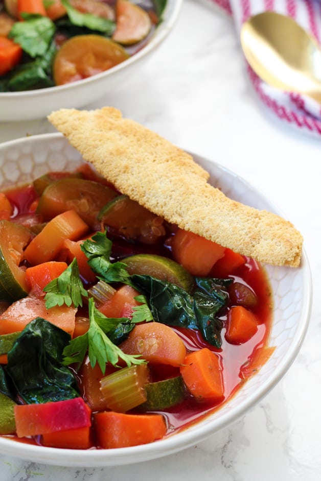 A bowl of minestrone soup with a cracker on it.