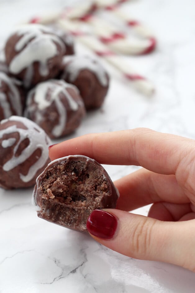 A hand holding a peppermint truffle with a bite taken out of it in front of a few other peppermint truffles sitting on a plate.