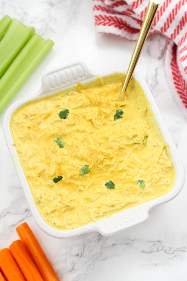 A white ceramic dish filled with buffalo chicken dip and a spoon in it and some celery next to it.