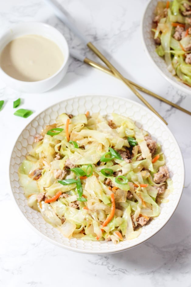 A white bowl filled with egg roll in a bowl and chop sticks nearby.