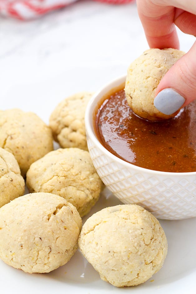 A hand dipping a pizza bite into red dipping sauce with other pizza bites next to the dipping sauce.