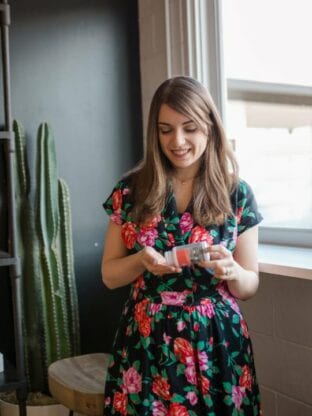 A photo of Michelle in a floral dress pouring some probiotics out into her hand from a bottle.