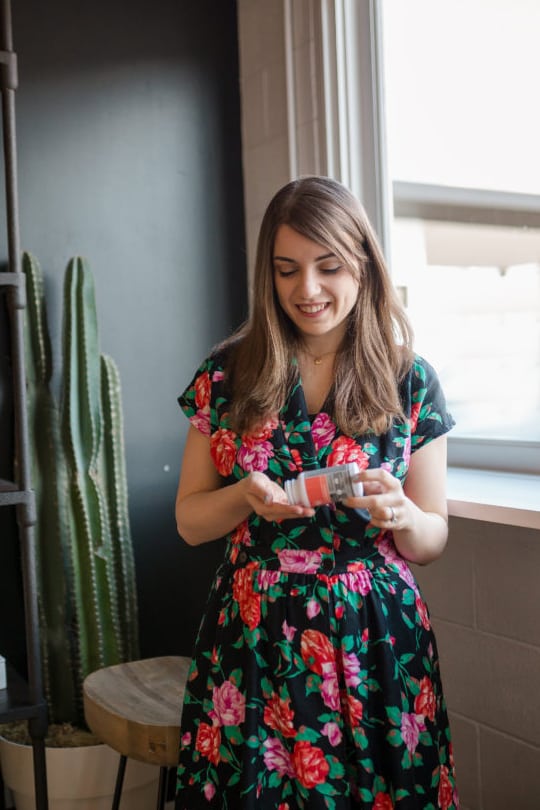 A photo of Michelle in a floral dress pouring some probiotics out into her hand from a bottle.