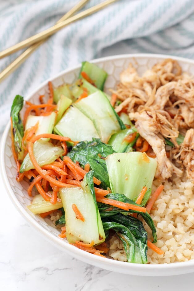 A white bowl filled with carrots and bok choy, cauliflower rice, and stir fry chicken.