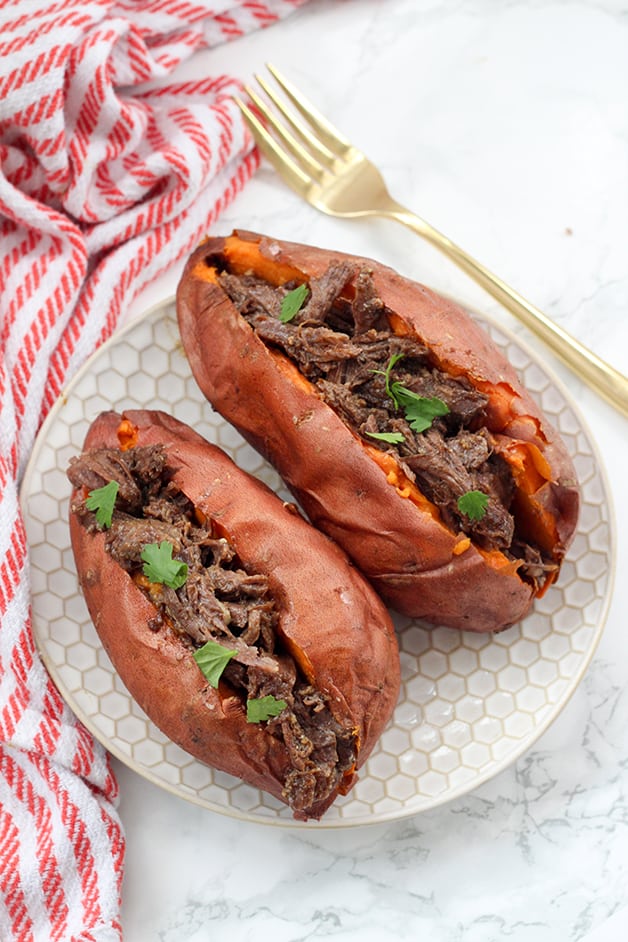 Two sweet potatoes on a plate stuffed with bbq beef and topped with fresh cilantro.
