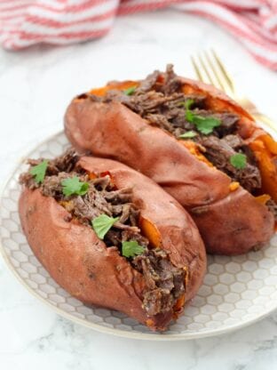 Two sweet potatoes on a plate stuffed with bbq beef and topped with fresh cilantro.