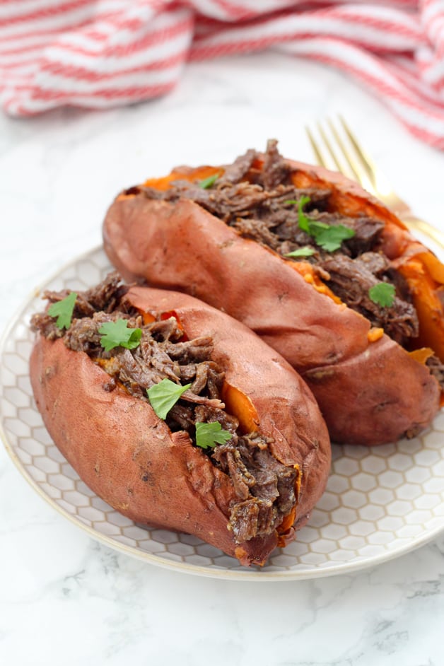 Two sweet potatoes on a plate stuffed with bbq beef and topped with fresh cilantro.
