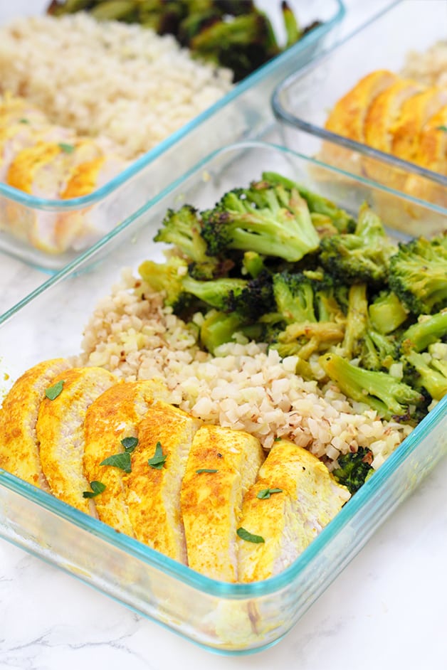 A glass meal prep container filled with turmeric chicken, cauliflower rice, and roasted broccoli.