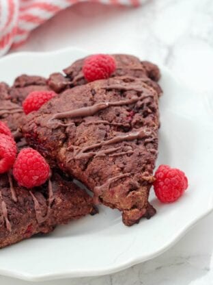 A white plate with paleo chocolate raspberry scones on it with fresh raspberries on top.